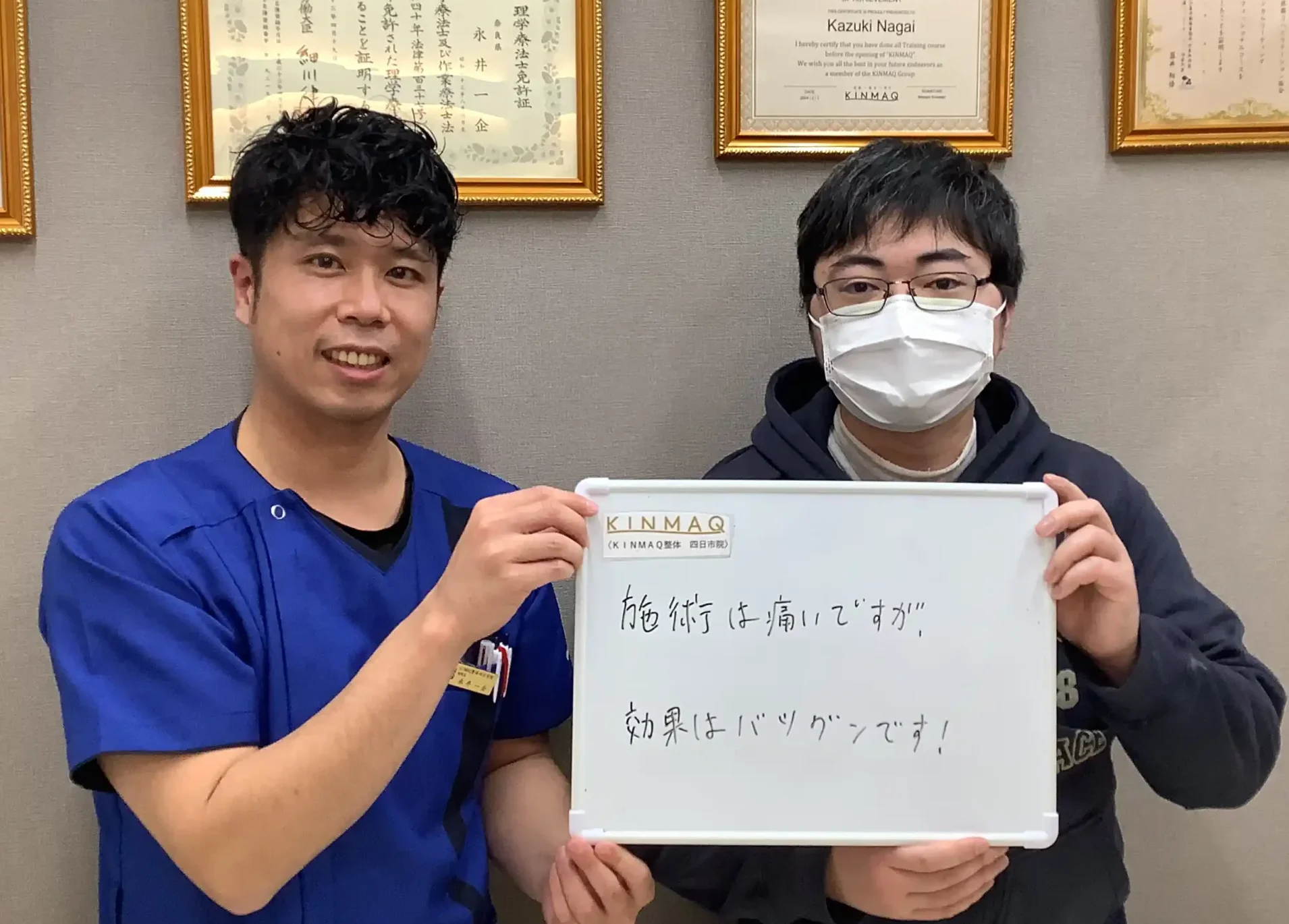 四日市の整体院で腰痛の改善のために通院していた男性の改善実績として。施術後のご本人と担当する理学療法士が一緒に『施術は痛いですが効果はバツグンです！』と書いたホワイトボードを持ち、担当した理学療法士と2ショットを撮影したときの写真。